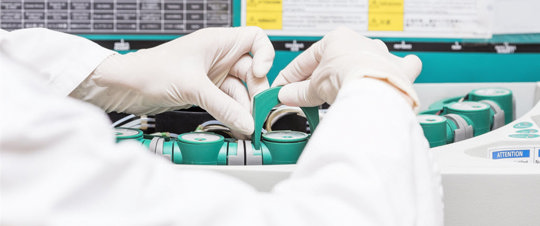 A person in a white lab coat operates a machine, focused on their task in a laboratory setting.